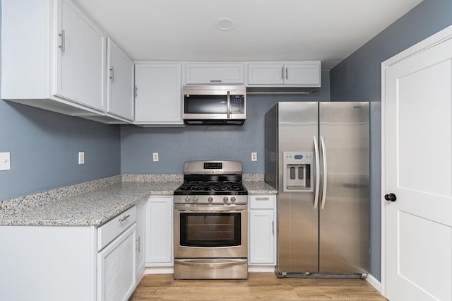 kitchen with appliances with stainless steel finishes, light wood-type flooring, white cabinetry, and light stone counters