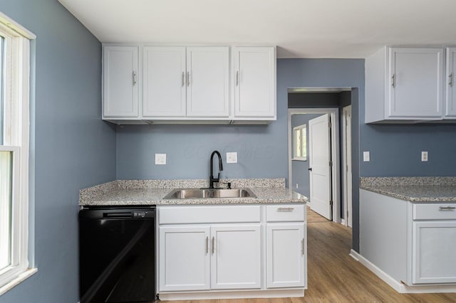 kitchen featuring dishwasher, a sink, light wood-style floors, white cabinets, and baseboards