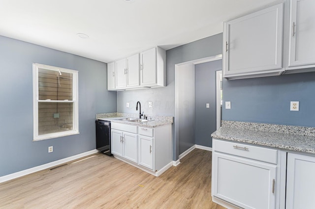 kitchen featuring a sink, black dishwasher, baseboards, light wood-style floors, and white cabinetry