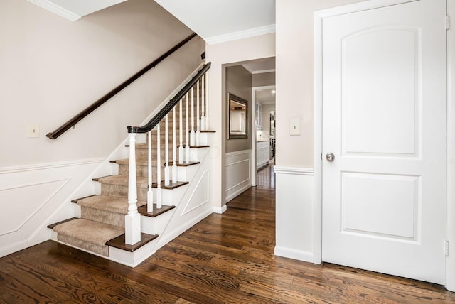 staircase with wood finished floors, ornamental molding, wainscoting, and a decorative wall