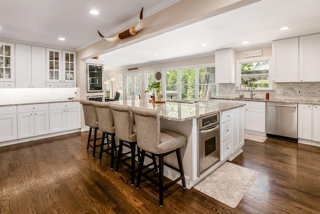 kitchen featuring appliances with stainless steel finishes, tasteful backsplash, a center island, ornamental molding, and white cabinetry