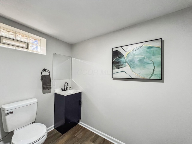 half bathroom featuring wood finished floors, toilet, vanity, and baseboards