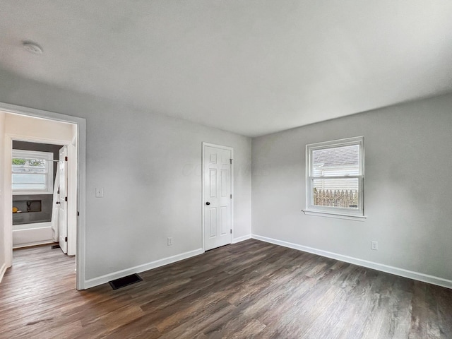 unfurnished bedroom with multiple windows, dark wood finished floors, and baseboards