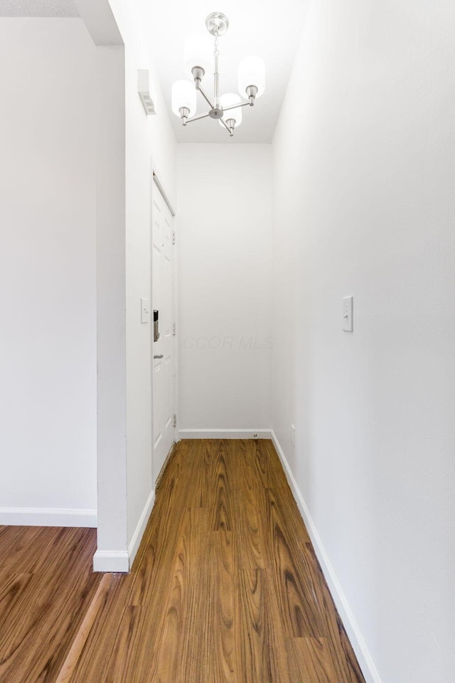 corridor featuring a chandelier, wood finished floors, and baseboards