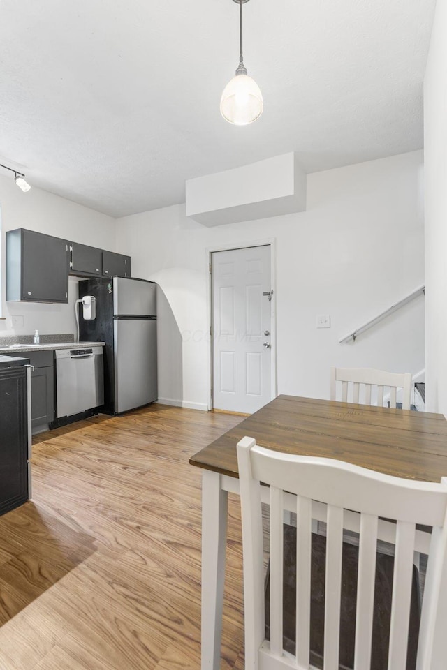 kitchen featuring stainless steel appliances, light wood-type flooring, light countertops, and hanging light fixtures