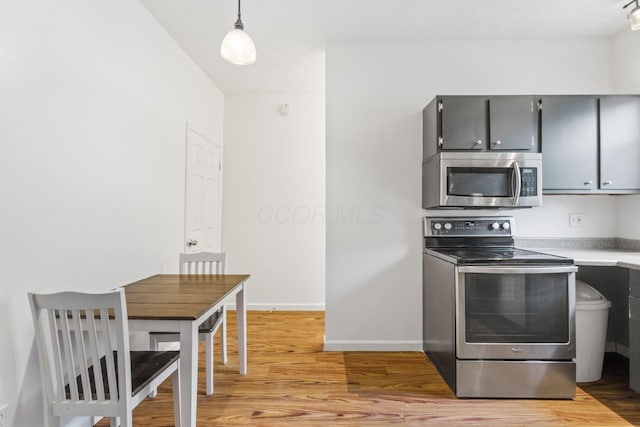 kitchen with stainless steel appliances, light wood finished floors, gray cabinets, light countertops, and baseboards