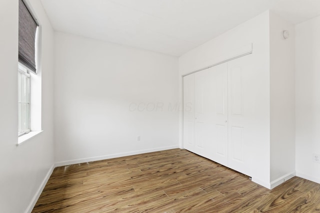 unfurnished bedroom featuring wood finished floors, a closet, and baseboards