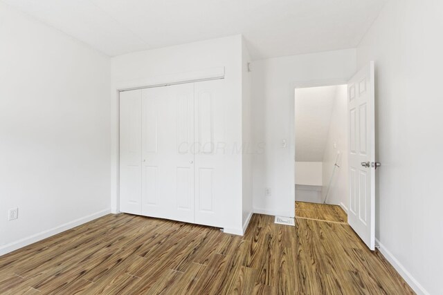 unfurnished bedroom featuring wood finished floors, a closet, and baseboards