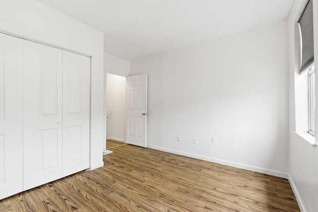 unfurnished bedroom with wood finished floors, baseboards, and a closet