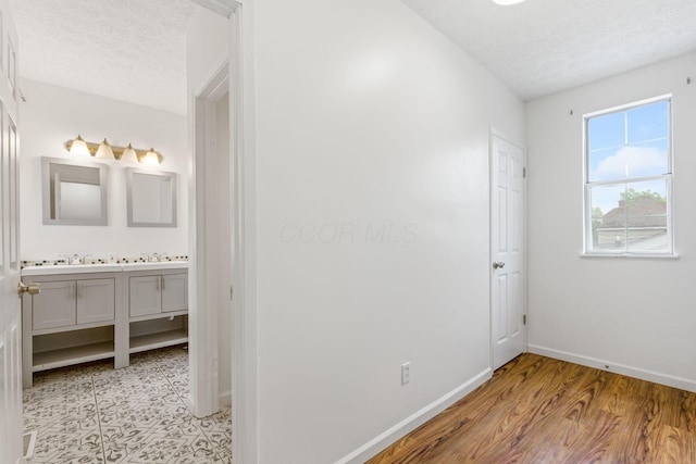 unfurnished bedroom featuring baseboards, a textured ceiling, ensuite bathroom, and light wood-style flooring