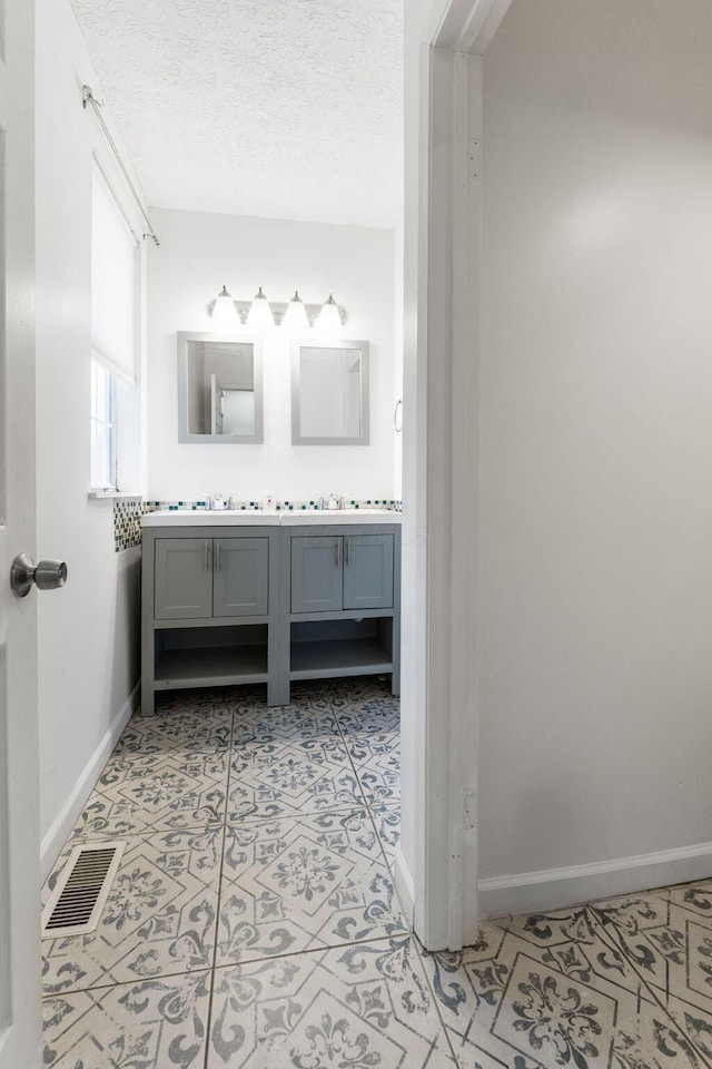 bathroom with baseboards, double vanity, and a textured ceiling