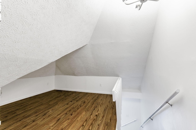 additional living space with a textured ceiling, dark wood finished floors, baseboards, and lofted ceiling