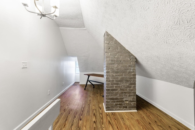 additional living space featuring a textured ceiling, lofted ceiling, baseboards, wood finished floors, and a chandelier