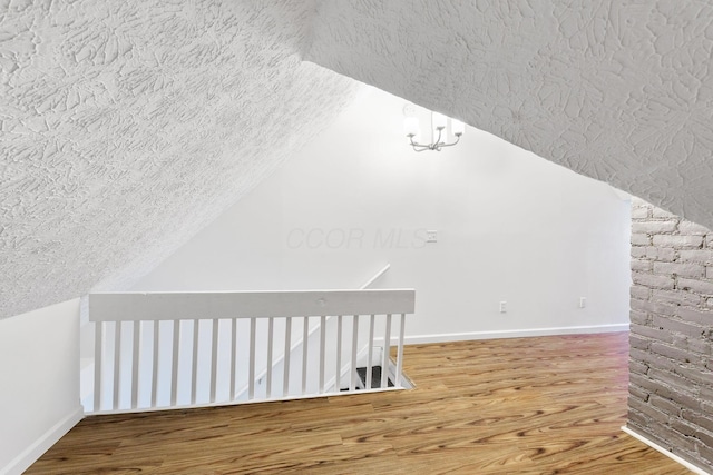 bonus room with a textured ceiling, wood finished floors, baseboards, and lofted ceiling
