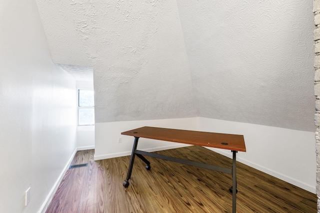 office area with a textured ceiling, wood finished floors, baseboards, and vaulted ceiling