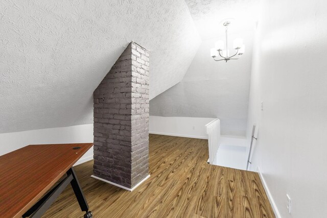 additional living space with a textured ceiling, wood finished floors, lofted ceiling, a chandelier, and baseboards