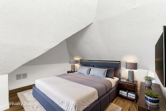 bedroom with a textured ceiling, wood finished floors, vaulted ceiling, and baseboards