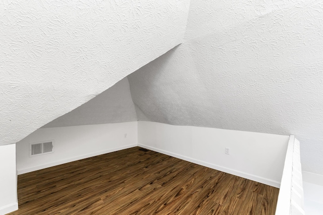 bonus room featuring a textured ceiling, dark wood finished floors, baseboards, and vaulted ceiling