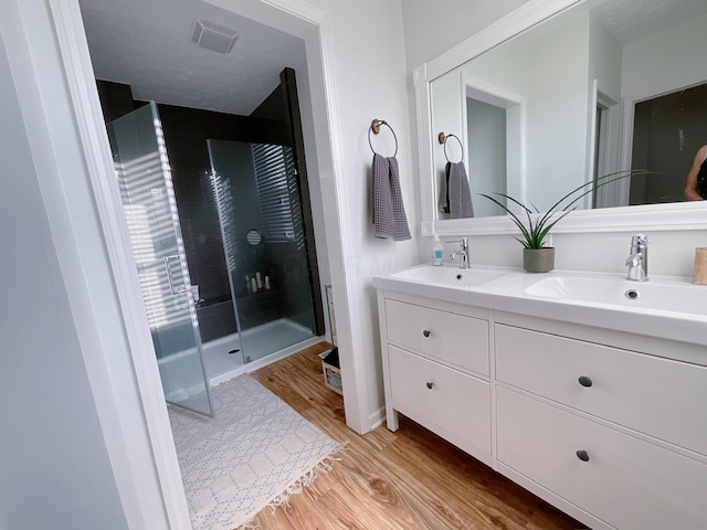 full bathroom with wood finished floors, a stall shower, and double vanity