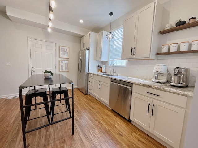 kitchen featuring appliances with stainless steel finishes, light wood-style floors, white cabinets, a sink, and tasteful backsplash