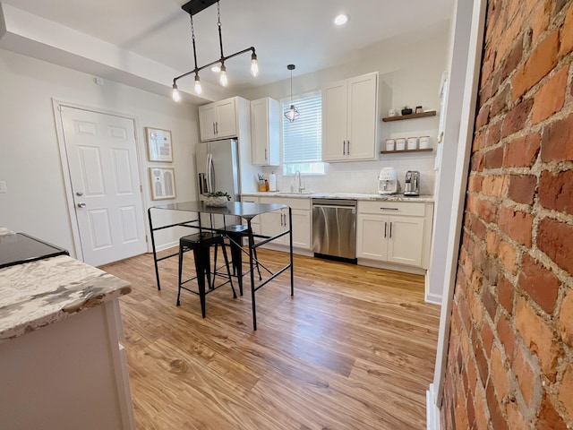 kitchen featuring stainless steel appliances, a sink, white cabinetry, light wood-style flooring, and pendant lighting
