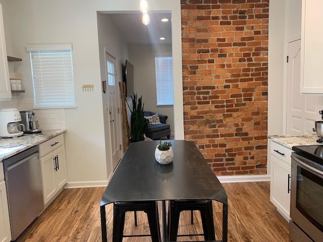 kitchen with appliances with stainless steel finishes, light wood finished floors, baseboards, brick wall, and white cabinets