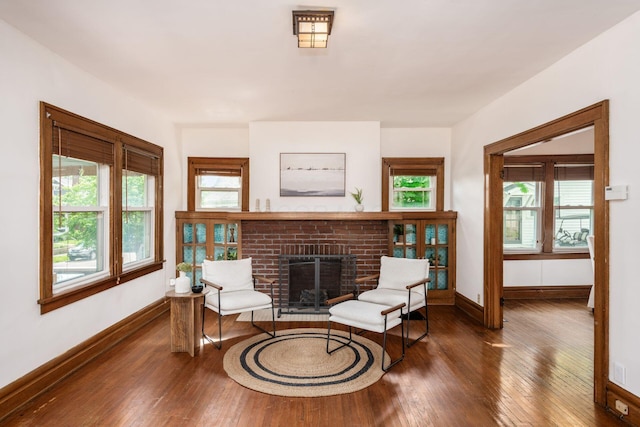 living area with baseboards, hardwood / wood-style flooring, a brick fireplace, and plenty of natural light