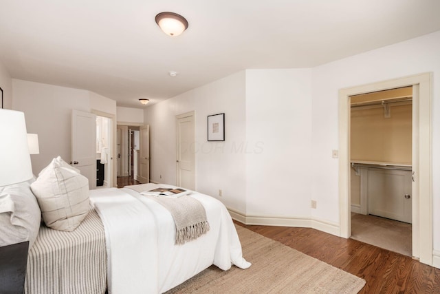 bedroom with wood finished floors, a walk in closet, baseboards, and a closet