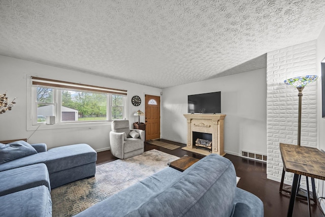 living area with wood finished floors, a fireplace with raised hearth, a textured ceiling, and baseboards