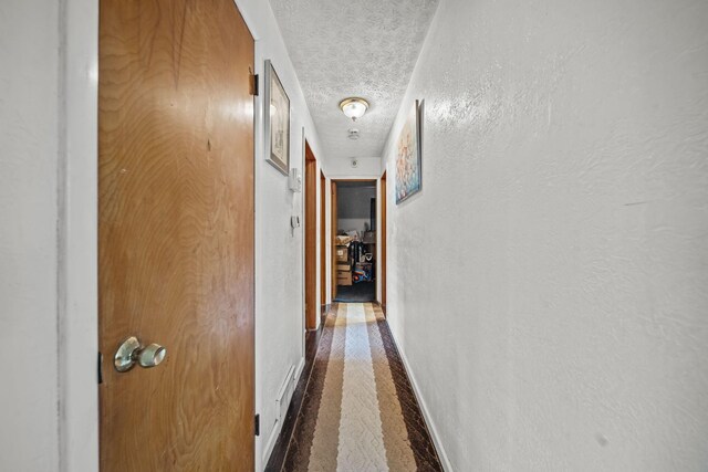 hallway featuring baseboards, carpet, a textured ceiling, and a textured wall