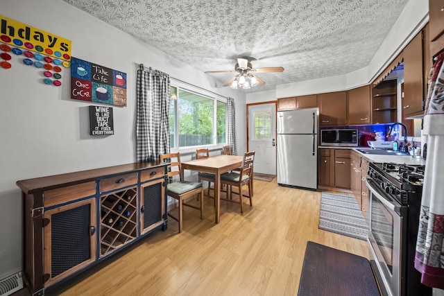 kitchen featuring stainless steel appliances, a sink, a textured ceiling, ceiling fan, and light wood-type flooring