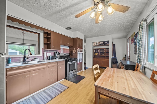 kitchen featuring gas stove, a sink, light wood-style floors, a ceiling fan, and tasteful backsplash