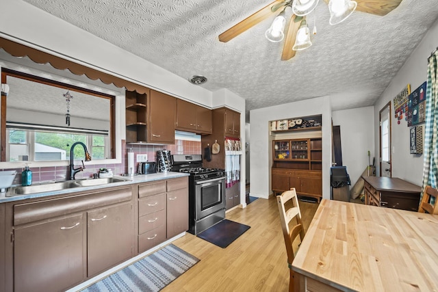 kitchen featuring stainless steel range with gas cooktop, a sink, light wood-style floors, tasteful backsplash, and open shelves