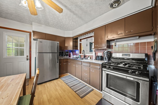kitchen with stainless steel appliances, a sink, open shelves, light wood-style flooring, and a textured ceiling