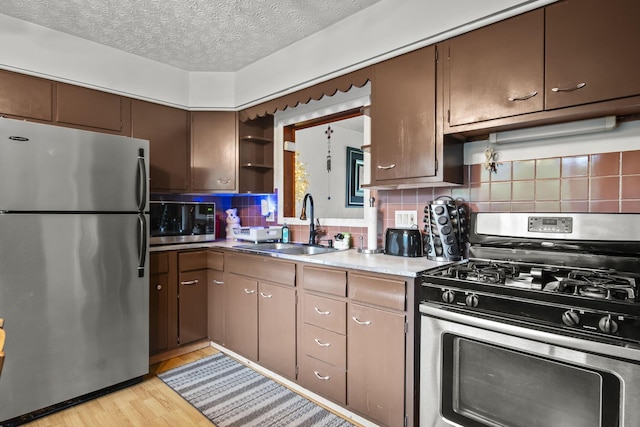 kitchen featuring appliances with stainless steel finishes, a sink, backsplash, light wood finished floors, and light countertops