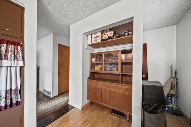 corridor with a textured ceiling, light wood-style floors, and baseboards