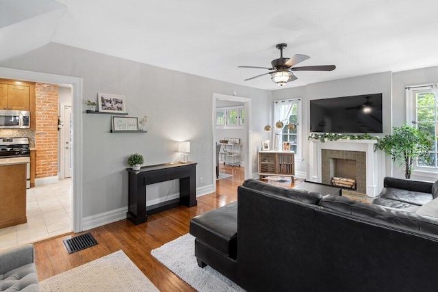 living area with a fireplace, a ceiling fan, baseboards, and light wood-style flooring