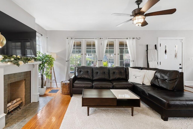 living area with a ceiling fan, wood finished floors, a tiled fireplace, and french doors
