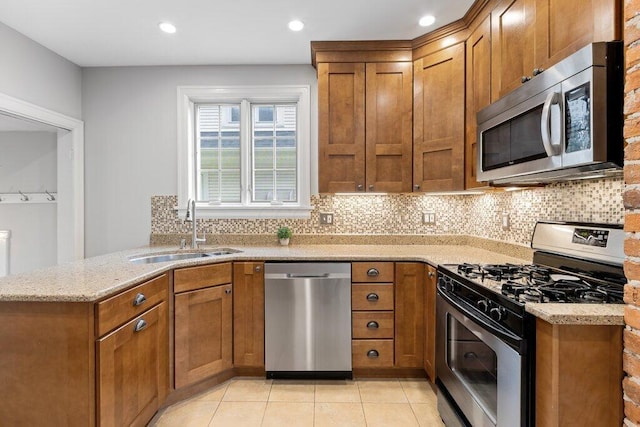 kitchen with stainless steel appliances, a sink, brown cabinets, decorative backsplash, and recessed lighting