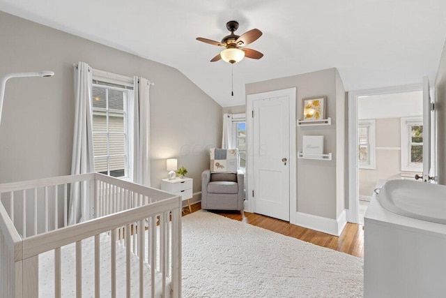 bedroom with wood finished floors, a nursery area, lofted ceiling, baseboards, and ceiling fan
