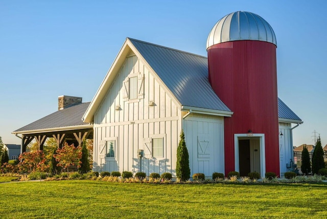 view of front of house with board and batten siding, a front lawn, a barn, and metal roof