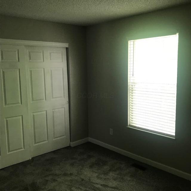 1817 Ridgebury Dr, Hilliard, OH 43026 - unfurnished bedroom with dark colored carpet, a textured ceiling, a closet, and baseboards