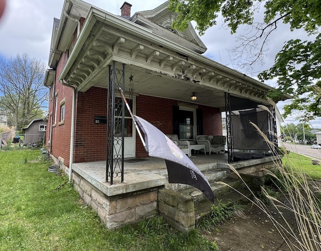 back of property featuring covered porch, a lawn, brick siding, and a chimney