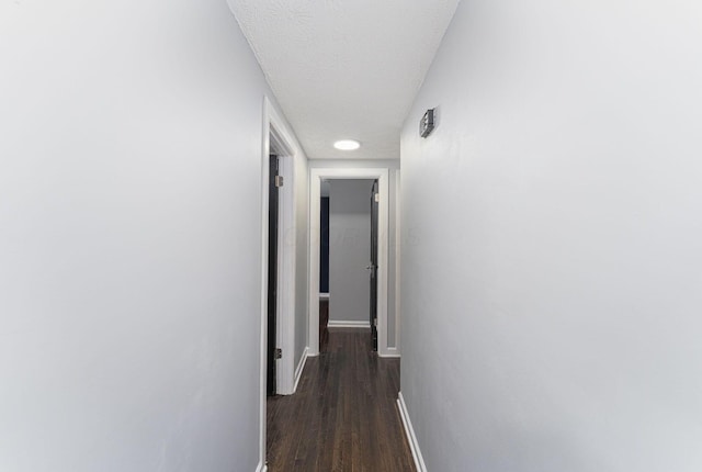 hallway with baseboards, dark wood-style floors, and a textured ceiling