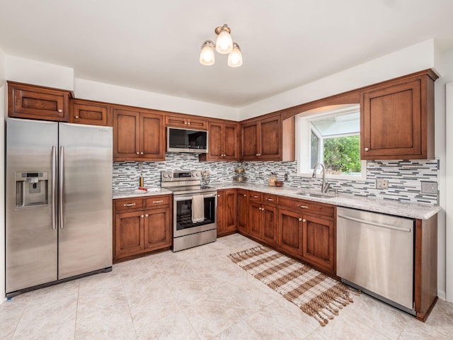 kitchen featuring stainless steel appliances, a sink, decorative backsplash, and light stone counters