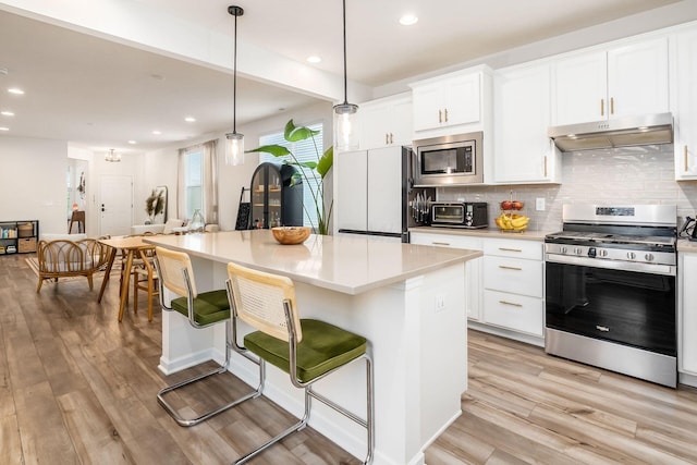 kitchen with stainless steel appliances, under cabinet range hood, recessed lighting, a kitchen bar, and backsplash