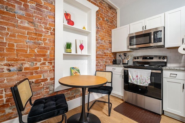 453-455 S 22nd St, Columbus, OH 43205 - kitchen with stainless steel appliances, light wood finished floors, white cabinetry, light stone countertops, and brick wall