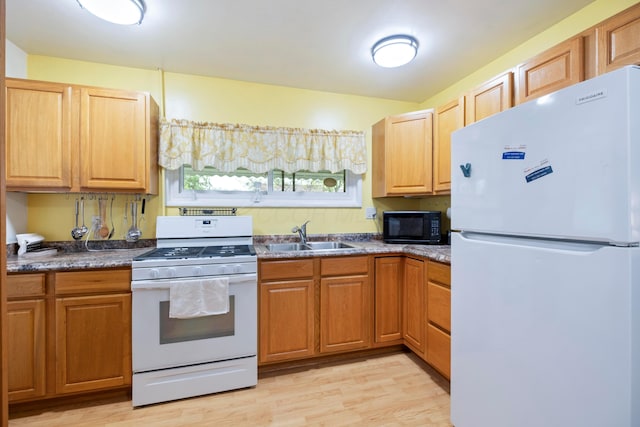 kitchen featuring white appliances, a sink, light wood finished floors, and dark countertops