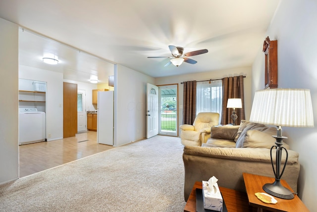 living area featuring washer / clothes dryer, light colored carpet, a ceiling fan, and baseboards