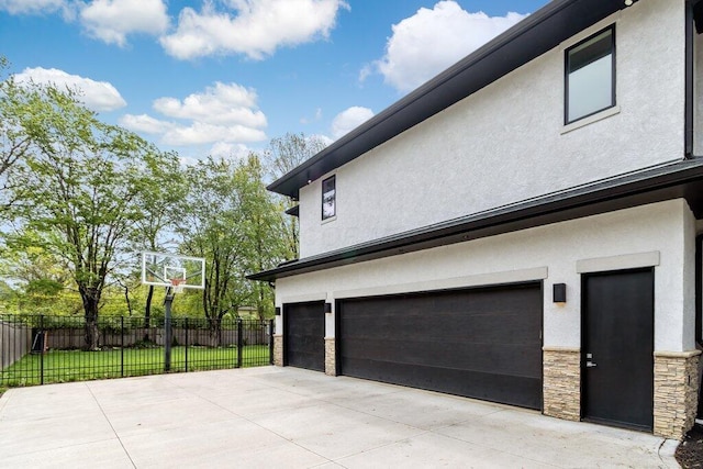 3084 Asbury Dr, Columbus, OH 43221 - view of home's exterior with stucco siding, fence, an attached garage, stone siding, and concrete driveway